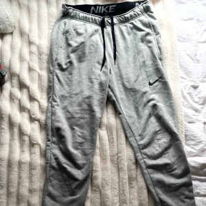 Grå mjukisbyxor från Nike - Grå mjukisbyxor från Nike med svart snörning i midjan och Dri-FIT-teknologi. Byxorna har elastisk midja. Perfekta för chill eller träning och riktigt sköna. Bara använda några gånger.