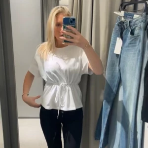 Vit t-shirt med snörning i midjan från Zara  - Säljer en fräsch vit t-shirt med korta ärmar och snygg snörning i midjan ifrån Zara, jag köpte för 300kr 