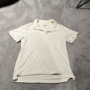 Vit frotté t-shirt med krage Kappahl - Vit t-shirt från Kappahl i storlek 134/140, tillverkad i mjuk frotté. Den har klassisk krage och korta ärmar, perfekt för en chill och avslappnad stil. Passformen är normal och materialet känns skönt mot huden.