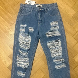 Blå oversized ripped jeans  - Trendiga slitna jeans i ljusblå denim. Jeansen har flera större slitningar fram som ger en tuff och edgy streetstil. De sitter lite lösare i passformen, vilket gör dem både bekväma och moderna. Perfekt att bära med sneakers och en hoodie eller med klackar och topp för en kontrastfull look.  De är helt nya med prislapp kvar och i perfekt skick.