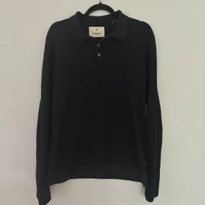 Svart pikétröja från Jack & Jones - Klassisk svart långärmad pikétröja från Jack & Jones Premium. Tröjan har krage, tre knappar framtill och är tillverkad i ett mjukt stickat material. Perfekt för dig som gillar en stilren och enkel look.