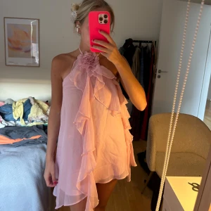 Rosa volangklänning med blomdetalj - Supersöt rosa kortklänning med volanger och stor blomma vid halsen. Från shein och aldrig använd 