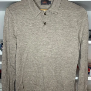 Beige långärmad pikétröja i merinoull från Morris - Stilren beige pikétröja från Morris i 100% merinoull. Tröjan har klassisk krage, två knappar framtill och lång ärm. Perfekt för dig som gillar en clean och tidlös look med premiumkänsla.