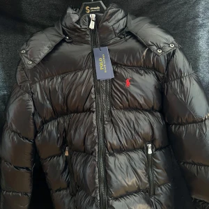 Glossed jacka Polo Ralph Lauren - Svart, glansig pufferjacka från Polo Ralph Lauren. Helt ny st:M