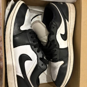 Nike Air Jordan 1 Low svart/vit - Säljer ett par Nike Air Jordan 1 Low i svart och vitt skinn. Klassisk siluett med svart swoosh, snörning och broderad Air Jordan-logga på hälen. Perfekta sneakers för dig som gillar streetstyle och vill ha en ikonisk look.