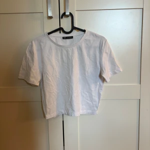 Vit croppad t-shirt från Zara - Enkel och stilren vit croppad t-shirt från Zara. Modellen har rund halsringning och korta ärmar. 