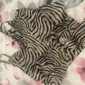 Zebramönstrad bikini med knyt - Snygg bikini med zebramönster i svart och beige. Toppen har smala axelband och knyt i ryggen för en justerbar passform. Materialet känns lätt och smidigt, perfekt för strandhäng. Bikinin har en trendig look som sticker ut.