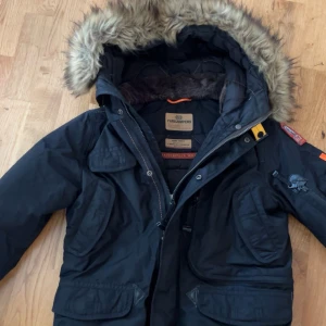 Xs/164 Svart vinterjacka Parajumpers med pälskrage - Grym svart vinterjacka från Parajumpers med stor huva och fet pälskant. Jackan har flera fickor, coola detaljer som gul rem och patch på ärmen. Perfekt för kalla dagar och riktigt snygg streetstil.