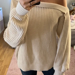 Beige offshoulder stickad tröja - Säljer en beige stickad tröja med offshoulder-design och bred ribbstickning. Tröjan har långa ärmar och en avslappnad passform, perfekt för dig som gillar en chill och trendig stil. Superenkel att matcha med jeans eller kjol💕