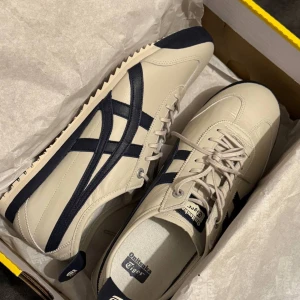 Onitsuka Tiger Mexico 66 sneakers - Snygga Onitsuka Tiger Mexico 66 sneakers i beige med marinblå detaljer. Klassisk retrodesign med låg profil, rund tå och snörning. Tillverkade i skinn med kontrasterande ränder på sidorna och platt sula. Perfekta för dig som gillar stilrena och tidlösa sneakers. Jag bar dem bara en gång.