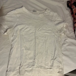 Vit t-shirt med broderad detalj - Vit t-shirt från BRONX med korta ärmar och snygg broderad detalj över bröstet. Rund halsringning och mjukt bomullsmaterial som känns skönt mot huden. Perfekt för dig som gillar stilrena plagg med en twist.