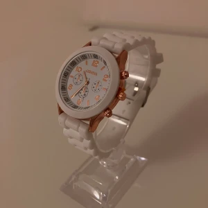 Vit klocka från Geneva med roséguld - Stilren klocka från Geneva med vit urtavla och armband i vit plast. Klockan har detaljer i roséguld, inklusive siffror, visare och knappar. Rund form och sportig look med flera små urtavlor på insidan. Perfekt accessoar för att lyfta din outfit.                                ✅Frakt inom 24 timmar 📦.                                                      ✅Nytt Batteri 🔋.