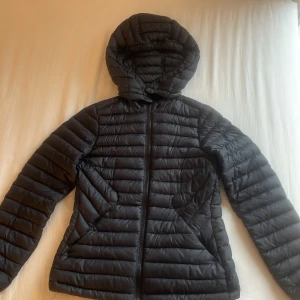 Svart pufferjacka från Sail Racing XS - Säljer en svart pufferjacka från Sail Racing i storlek XS. Jackan har huva, hel dragkedja och är quiltad med horisontella sömmar. Perfekt för kyliga dagar och har en clean look.. Materialet är syntet och jackan är lätt och smidig att bära.