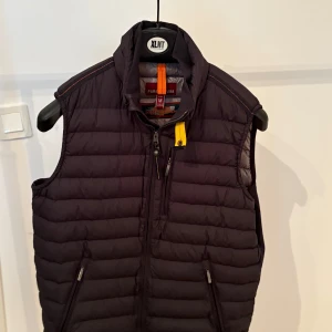 Svart dunväst från Parajumpers M - ÄKTA Snygg svart dunväst från Parajumpers i superlätt material. Västen har ståkrage, dragkedja framtill, tre fickor med dragkedja och en gul detalj vid halsen. Perfekt att slänga över en hoodie eller tröja för extra värme. PRIS KAN DISKUTERAS 