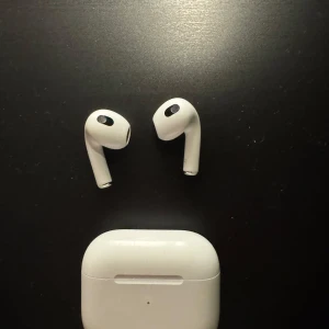 AirPods 3 - Apple AirPods 3 med laddningsetui. Trådlösa hörlurar med bra ljudkvalitet och smidig anslutning till Apple-enheter. Mindre repor och normalt slitage syns på etuiet, men hörlurarna är i gott skick och fungerar utmärkt.
