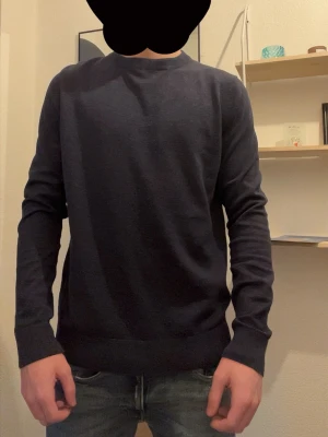 Mörkblå rundhalsad tröja - En stilren mörkblå tröja med rund halsringning och långa ärmar. Tröjan har en smal passform och ribbade muddar vid ärmslut och nederkant. Perfekt att matcha med jeans för en clean look.