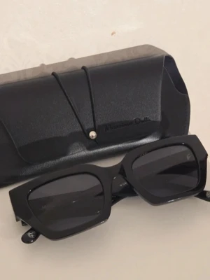 Svarta solglasögon Massimo Dutti - Stilrena svarta solglasögon från Massimo Dutti med rektangulära bågar och mörka glas. Kommer med ett matchande svart fodral med logga. Perfekta för dig som gillar en klassisk och trendig look.
