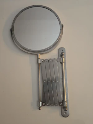 Väggmonterad sminkspegel i metall - Snygg rund sminkspegel i silverfärgad metall med utfällbar arm som gör det enkelt att justera avståndet. Perfekt för sminkning eller hudvård. Spegeln är stilren och passar i de flesta badrum.