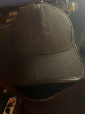 Svart keps från Gucci med GG-mönster - Snygg svart keps från Gucci med klassiskt GG-mönster över hela kepsen. Justerbar rem baktill i skinn med präglad Gucci-logga. Perfekt accessoar för att lyfta din streetwear-look.