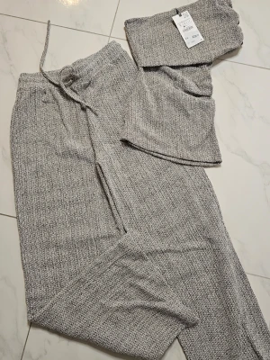 Gråmelerat loungewear-set H&M - Mysigt loungewear-set från H&M i gråmelerad färg. Setet består av ett par byxor med dragsko i midjan och en matchande topp. Materialet är mjukt och stretchigt, perfekt för chill dagar hemma. Enkel och avslappnad passform.