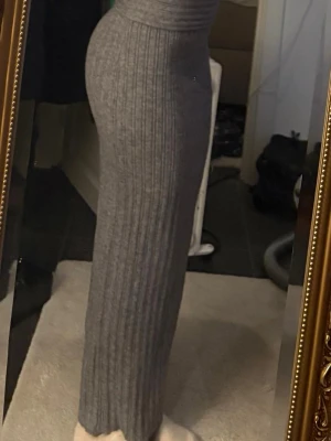 Grå ribbad långkjol i stickat material - Snygg grå långkjol i ribbstickat material med hög midja. Kjolen är figurnära och har en klassisk, enkel design som passar perfekt till många olika stilar.