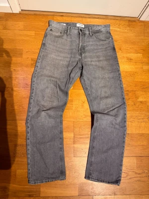 Grå raka jeans från Jack and Jones - Säljer ett par grå jeans från Jack and Jones med rak passform och klassisk femficksdesign. Jeansen har normal midja och är tillverkade i denim. Perfekta för en avslappnad och stilren look. Knappt andvända