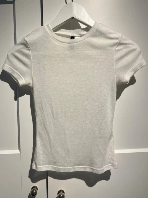 Vit basic t-shirt från H&M - En enkel och stilren vit t-shirt från H&M. Modellen har rund halsringning och korta ärmar. Tillverkad i mjuk bomull som känns skön mot huden. Perfekt att matcha med jeans eller kjol för en clean look.