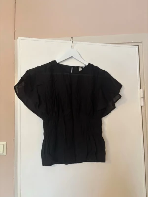 Svart blus med vida ärmar - Snygg svart blus med jättefin passform och vida, korta ärmar. Blusen har smockdetaljer i midjan som ger en markerad siluett 