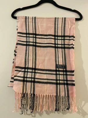 Klassisk Burberry Halsduk - Burberry halsduk 🤍🩷  Klassisk Burberry-halsduk i det välkända rutmönstret. En tidlös favorit som aldrig går ur stil.  ✨ Detaljer: – Material: Lammull – Färg: Rosa/Vit/Svart – Mått: 167 cm x 32 cm – Skick: Mycket bra – Original: Ja  Perfekt till höst & vinter och funkar både casual och uppklätt. Skickas snabbt 📦  Pris kan diskuteras. 