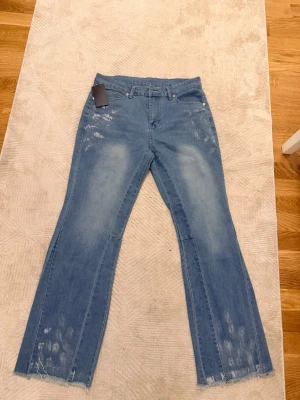 Ljusblå flared jeans med slitningar - Säljer ett par ljusblå jeans med slitna detaljer och råa fållar. Jeansen har en relaxed wide passform och hög midja, perfekta för en chill och trendig look. Klassisk femficksmodell i mjukt bomullsjeansmaterial.
