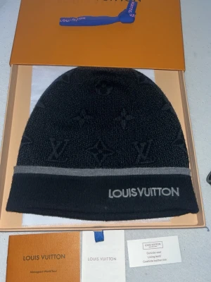 Svart mössa från Louis Vuitton - Snygg svart mössa från Louis Vuitton med diskret monogrammönster och grå kant. Märkets logga är broderad framtill. Tillverkad i ull och fodrad med mjukt material för extra komfort. Perfekt accessoar för dig som vill ha en exklusiv och stilren look.
