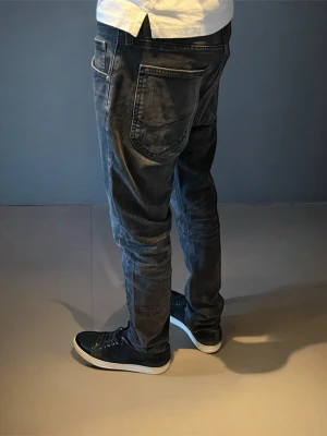 Svarta slimfit jeans från Lee - Säljer ett par svarta slimfit jeans från Lee med tvättad look. Modellen är Luke. Jeansen har en avslappnad passform och klassisk femficksdesign. sopass coola till sneakers och t-shirt. Materialet är denim i bomull. Storleken är W31 L32. Skriv vid fler frågor