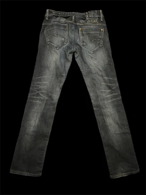 G-Star raka blå jeans - Säljer ett par klassiska blå jeans från G-Star med raka ben och slitna detaljer. Jeansen har fem fickor, kontrastsömmar och logotyp på bakfickan. Tillverkade i denim med en snygg tvättad look och subtila slitningar för en avslappnad stil.