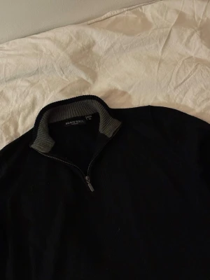 Svart stickad halfzip   - Svart stickad tröja från Brave Soul i storlek XS med halv dragkedja och ribbad krage i grått. Långärmad modell med ribbade muddar vid ärmslut och nederkant. Perfekt för lager på lager och enkel att matcha.