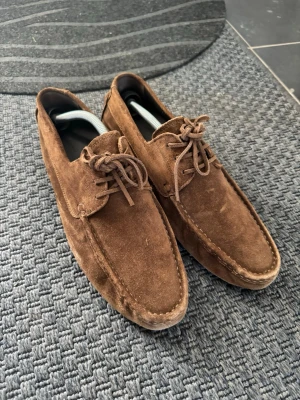 Bruna mocka loafers ifrån Massimo dutti - Säljer ett par bruna loafers i mocka med klassisk snörning framtill. Skorna har en stilren design med rundad tå och synliga sömmar längs kanterna. Perfekta för dig som gillar en avslappnad men ändå snygg stil.