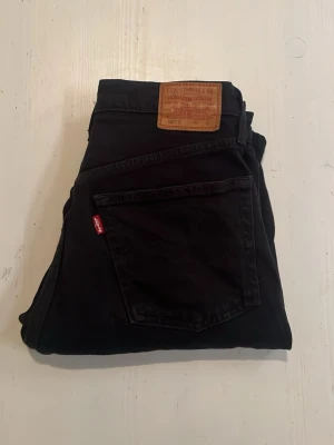 Svarta Levi's jeans med rakt ben - Säljer ett par klassiska svarta jeans från Levi's med rakt ben och femficksmodell. Jeansen har den ikoniska röda Levi's-lappen på bakfickan och patch i läder bak i midjan. Tillverkade i slitstark denim som passar till många olika stilar.
