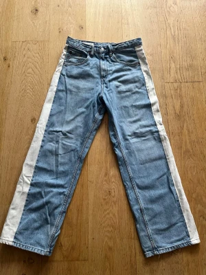 Blå jeans med vita sidor från Zara - Säljer ett par ljusblå raka jeans från Zara med breda vita paneler längs båda sidorna. Storlek W30 L32. Byxorna har en mer baggy passform. Bra skick, endast lite slitage vid benöppningen. Skriv om du har några frågor! Priset går att diskutera!