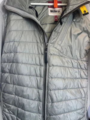 Ljusgrå dunväst från Parajumpers - Snygg ljusgrå dunväst från Parajumpers med quiltad design och hög krage. Västen har dragkedja framtill och den klassiska gula Parajumpers-detaljen vid halsen. Perfekt för lager-på-lager och håller dig varm under kyliga dagar.