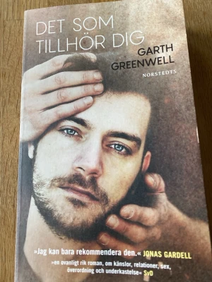 Det som tillhör dig av Garth Greenwell - En roman med mjukpärm i bruna och beige toner. Boken handlar om kärlek, relationer och identitet, och utspelar sig i Sofia, Bulgarien. Omslaget har ett konstnärligt foto av två händer och text i vitt. Perfekt för dig som gillar starka berättelser om känslor och relationer.