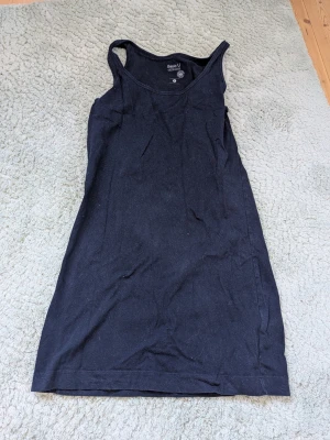 Svart nattlinne från Basic U - Ett enkelt svart nattlinne från Basic U i mjukt bomullsmaterial. Modellen är ärmlös med rund halsringning och rak passform, perfekt för en avslappnad och bekväm känsla på natten.