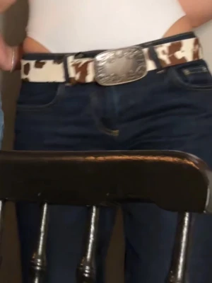 Cowboybälte med silverdetalj - Snyggt cowboyinspirerat bälte med brunt och vitt mönster samt en stor, graverad silverspänne. Perfekt accessoar för att lyfta din outfit med western-vibe. Bältet har ett coolt mönster som sticker ut och passar till jeans.