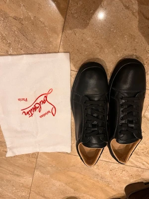 Svarta sneakers från Christian Louboutin - Stilrena svarta sneakers i läder från Christian Louboutin med klassisk röd sula och svarta skosnören. Låg modell med diskret design och exklusiv känsla. Dustbag till skorna samt certifierings kort ingår. Perfekta för dig som vill ha något lyxigt och tidlöst i garderoben.