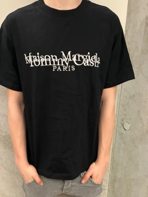 Maison Margiela x Tommy Cash svart t-shirt - Sällsynt Masion margiela X Tommy cash T-shirt i färgen svart. Tröjan är storlek S och har klassisk passform och är knappt använd. Stilren och snygg. Hör av er vid frågor! 