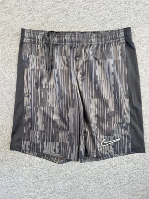 Svarta Nike shorts med mönster - Snygga svarta shorts från Nike med grått grafiskt mönster och Nike-logga framtill. Shortsen har elastisk midja med dragsko och meshpaneler på sidorna för extra ventilation. Perfekta för träning eller chill.