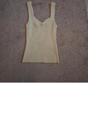 Ribbad beige ärmlös topp - Trendig ribbad topp i beige med breda axelband och markerad byst. Snygg passform och stretchigt material som sitter skönt. Perfekt att styla med jeans eller kjol för en cool look.