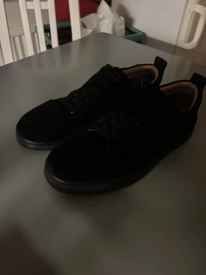 Christian Louboutins - Snygga svarta sneakers med lågt skaft och cool röd sula med textdetalj undertill. Skorna har klassisk snörning och en stilren design som passar till det mesta. Perfekta för dig som gillar en clean look med en twist.