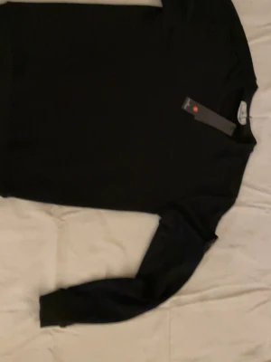 Svart tröja från Stone Island - Snygg svart tröja från Stone Island med rund hals och diskret design. Tillverkad i mjukt material som känns skönt mot huden. Perfekt för dig som gillar stilrena plagg med exklusiv känsla. Tröjan har långa ärmar och klassisk passform.