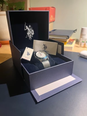 US Polo Assn herrklocka i silver - Säljer en stilren herrklocka från US Polo Assn med silverfärgat mesharmband och vit urtavla. Klockan levereras i originalförpackning med logga och tillhörande kort. Perfekt accessoar för dig som gillar klassisk design.