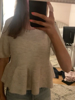 Beige peplum topp med kort ärm - Söt beige topp med peplumvolang och korta ärmar. Mjuk och skön, perfekt till jeans eller kjol. Rund halsringning och avslappnad passform ger en trendig look.