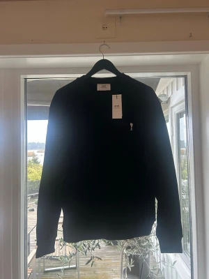 Svart sweatshirt från Ami Paris - Svart sweatshirt från Ami Paris med rund halsringning och det ikoniska Ami de Coeur-logotypen broderad på bröstet. Tröjan har långa ärmar och ribbade muddar vid ärmslut och nederkant. Perfekt för en stilren och avslappnad look.